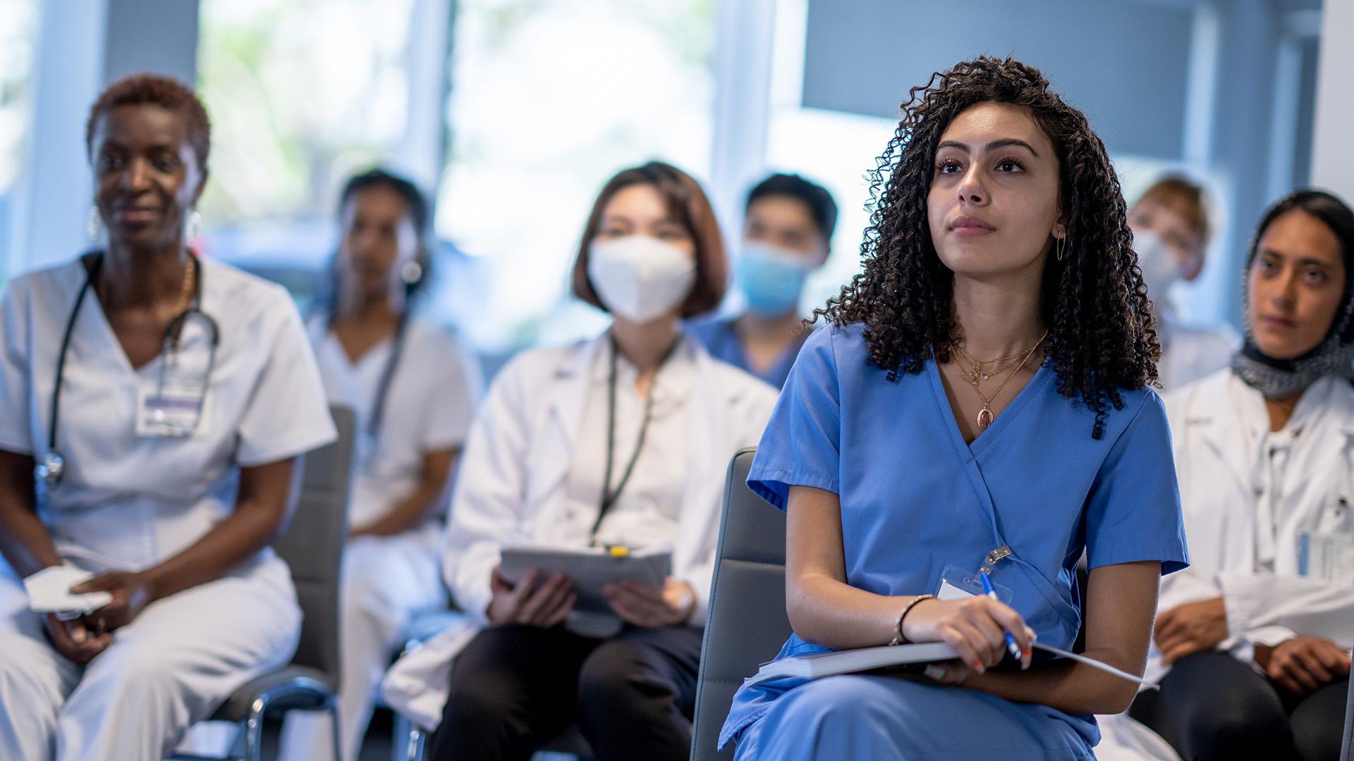 A diverse group of female medical students listen attentively while seated for a lecture.