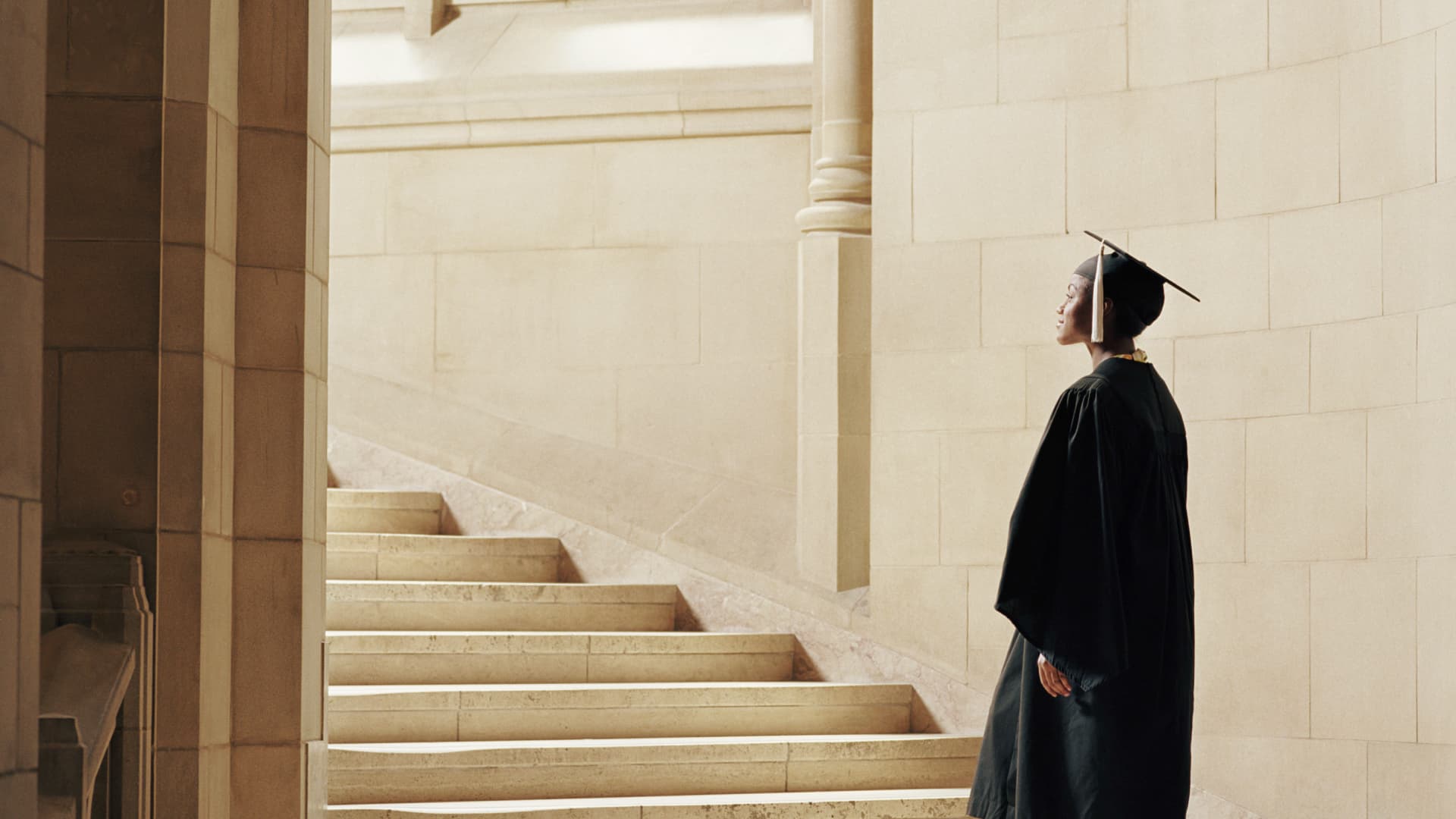 Woman wearing graduation cap and gown, ascending staircase, rear view